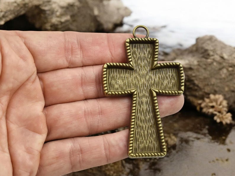 May include: A gold-toned metal cross pendant with a textured surface and a rope-like border. The cross has a loop at the top for hanging.