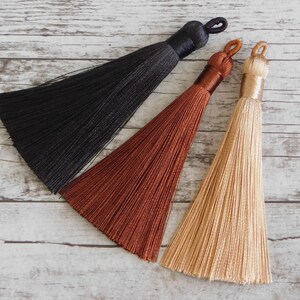 May include: Three tassels in black, brown, and beige. The tassels are made of soft, silky threads and have a simple, elegant design.