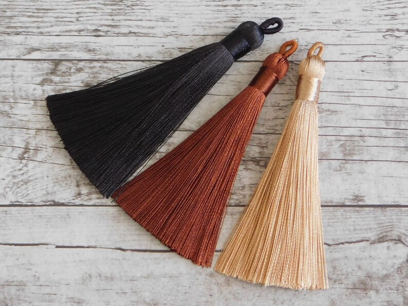 May include: Three tassels in black, brown, and beige. The tassels are made of soft, silky threads and have a simple, elegant design.