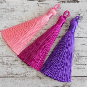 May include: Three silk tassels in pink, magenta, and purple colors. The tassels are made of soft, silky threads and have a delicate, elegant look.