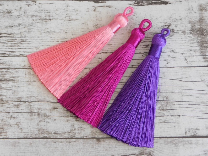 May include: Three silk tassels in pink, magenta, and purple colors. The tassels are made of soft, silky threads and have a delicate, elegant look.