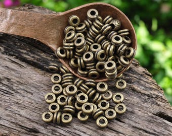 May include: A wooden spoon filled with antique gold metal beads. The beads are round with a raised line around the center. The spoon is sitting on a piece of weathered wood.