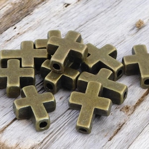 May include: A pile of antique gold-toned metal cross-shaped beads. The beads are approximately 2.5 cm in size and have a slightly textured surface.