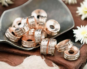 May include: A group of rose gold metal beads with a geometric design. The beads are arranged in a pile on a brown surface.