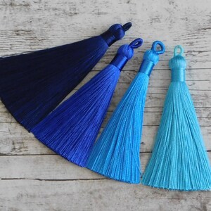 May include: Four silk tassels in shades of blue. The tassels are arranged in a row from darkest to lightest, with a navy blue tassel at the top and a turquoise tassel at the bottom.
