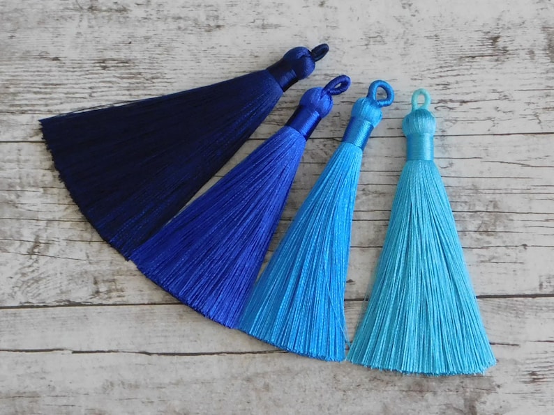 May include: Four silk tassels in shades of blue. The tassels are arranged in a row from darkest to lightest, with a navy blue tassel at the top and a turquoise tassel at the bottom.