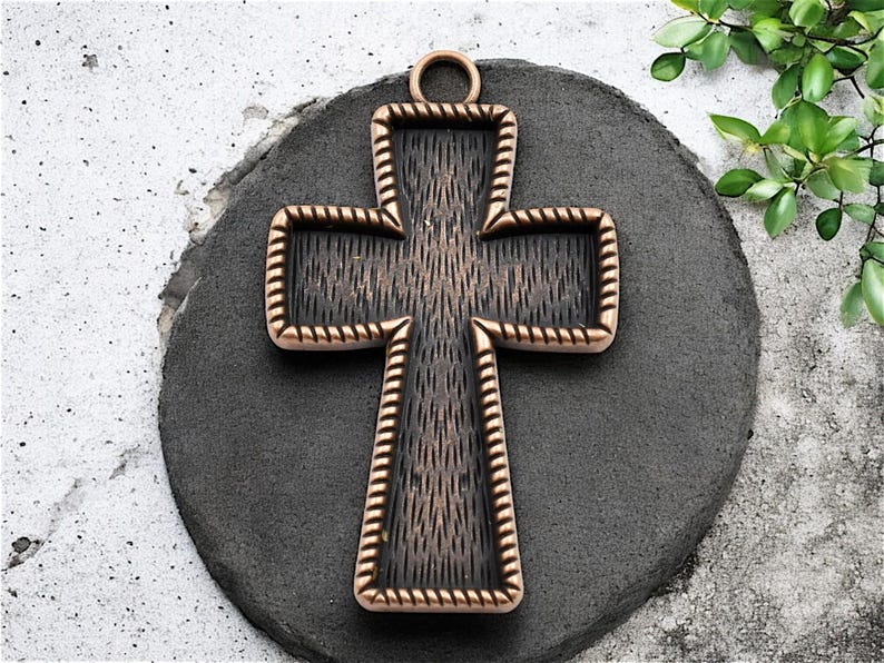 May include: A large, ornate, copper-colored cross pendant with a black, textured center. The cross has a rope-like border and a loop at the top for hanging.