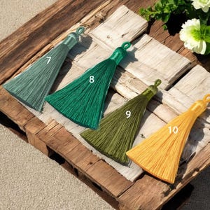 May include: Four different colored tassels with numbers 7, 8, 9, and 10 printed on them. The tassels are arranged in a row on a wooden surface.