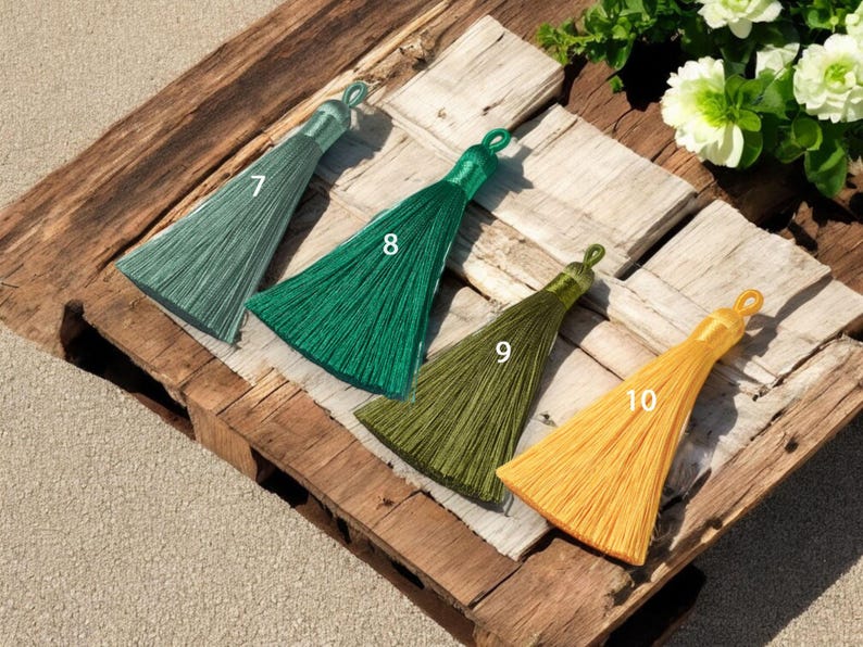 May include: Four different colored tassels with numbers 7, 8, 9, and 10 printed on them. The tassels are arranged in a row on a wooden surface.