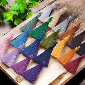 May include: Assortment of colorful silk tassels in various shades, including pink, purple, blue, green, yellow, orange, and red. The tassels are arranged on a wooden surface.