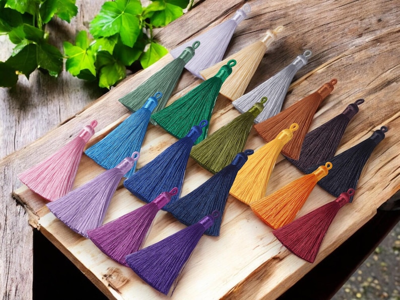 May include: Assortment of colorful silk tassels in various shades, including pink, purple, blue, green, yellow, orange, and red. The tassels are arranged on a wooden surface.