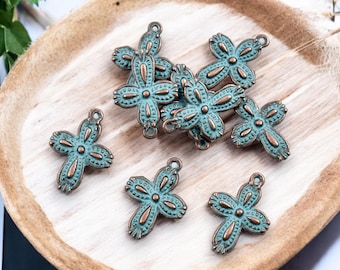 May include: A collection of antique-style cross charms with a turquoise and bronze finish. The charms are arranged on a wooden tray, showcasing their intricate floral design and small loop for attaching to jewelry or crafts.