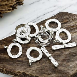 May include: A set of silver-toned metal jewelry findings, including round toggle clasps and jump rings. The findings have a hammered texture and are perfect for creating jewelry.