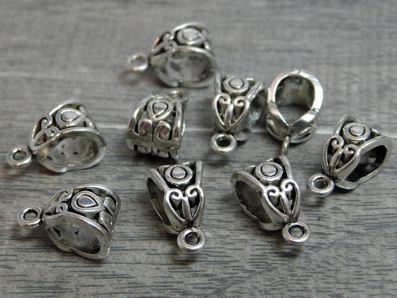 May include: Eight silver-toned metal pendant caps with ornate designs. The caps have a loop at the top for attaching to a chain or cord.