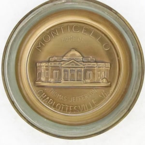 May include: A gold-colored metal coin with the words "MONTICELLO HOME OF THOMAS JEFFERSON CHARLOTTESVILLE VA" around the edge. The center of the coin features a raised image of Monticello, the home of Thomas Jefferson.
