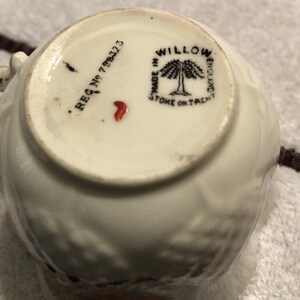 May include: Close-up of the bottom of a white teacup with a black and white willow tree design. The text "MADE IN STOKE ON TRENT" and "WILLOW WARE" are printed on the bottom of the cup. The registration number "REG No 793273" is also printed on the bottom of the cup.