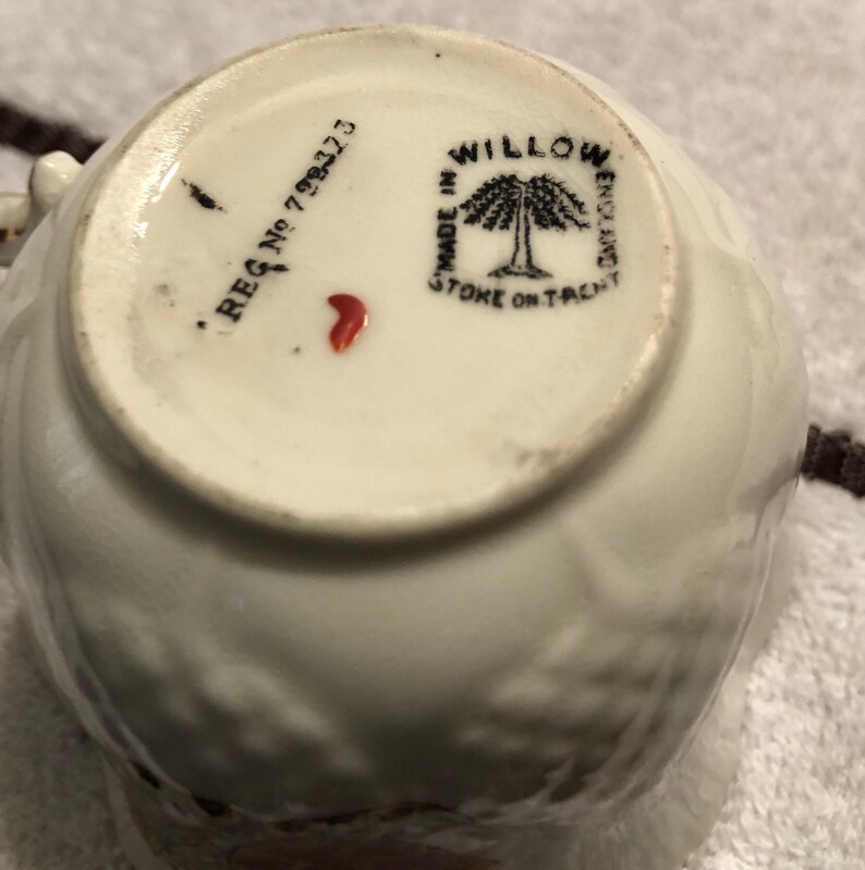 May include: Close-up of the bottom of a white teacup with a black and white willow tree design. The text "MADE IN STOKE ON TRENT" and "WILLOW WARE" are printed on the bottom of the cup. The registration number "REG No 793273" is also printed on the bottom of the cup.
