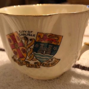 May include: A white teacup with gold trim and a crest featuring the words "City of Carlisle" and "Be Just and Fear Not".