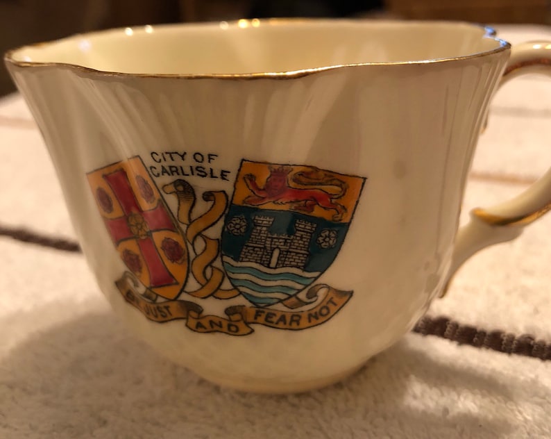 May include: A white teacup with gold trim and a crest featuring the words "City of Carlisle" and "Be Just and Fear Not".