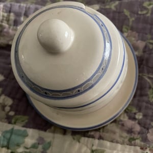 May include: A white ceramic butter dish with a blue and gray patterned design. The dish has a lid with a knob on top.