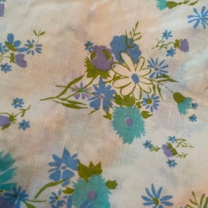 May include: White fabric with a floral pattern featuring blue, green, and purple flowers. The fabric has a subtle linen texture.