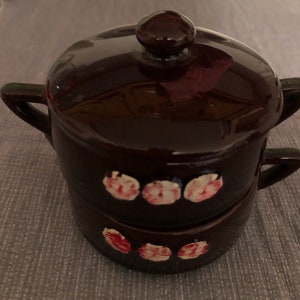 May include: A set of two brown ceramic pots with lids. The pots have a white and pink floral design.