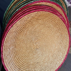 May include: A stack of woven placemats. Each round mat has a natural tan center with a braided red or green border. The mats are made of a natural fiber and are suitable for dining.