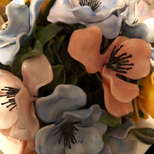 May include: A bouquet of artificial flowers with blue, pink, and yellow petals. The flowers have black centers and are arranged in a cluster.