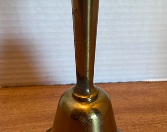 May include: A gold-colored metal bell with a long handle. The bell has a smooth, polished surface.