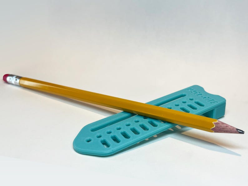 May include: A yellow pencil with a pink eraser rests on a teal-colored pencil holder. The pencil holder has a series of rectangular cutouts and the text "Paper-Mate" printed on it. The pencil is sharpened and ready for use.
