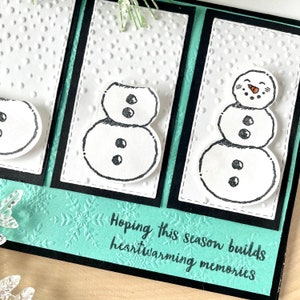 Może przedstawiać: Turkusowa kartka z białym tłem i trzema czarno-białymi ilustracjami bałwan&oacute;w. Kartka ma czarną ramkę, a tekst "Hoping this season builds heartwarming memories" jest napisany czarnym, ozdobnym pismem.