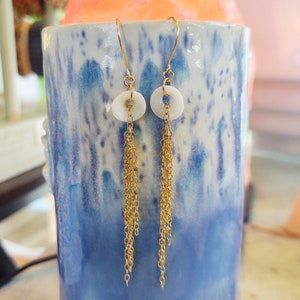 May include: A pair of gold earrings with white circular pendants and dangling gold chains.