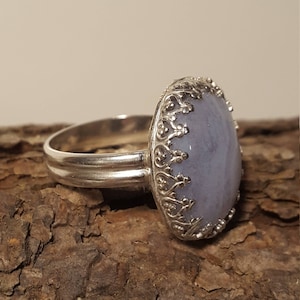 May include: A silver ring featuring a light blue oval gemstone set in an ornate silver bezel. The ring has a wide band.
