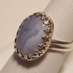 May include: A silver ring featuring a light blue and white agate stone set within a floral design.