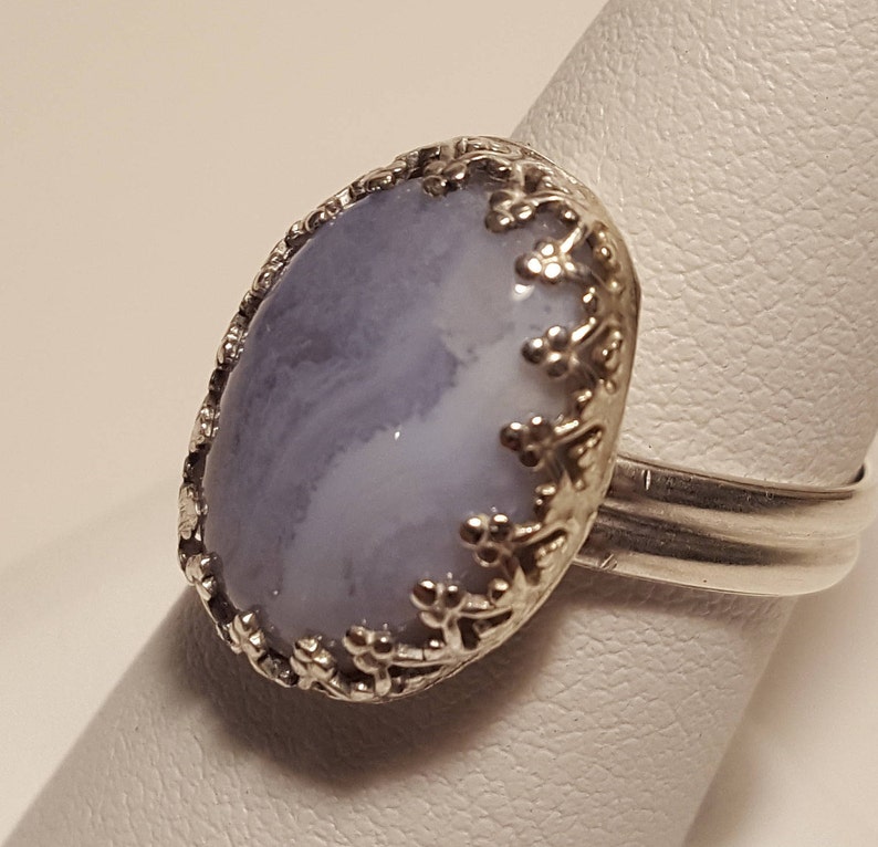 May include: A silver ring featuring a light blue and white agate stone set within a floral design.