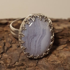 May include: A silver ring featuring a delicate floral design encircling a light blue agate stone.
