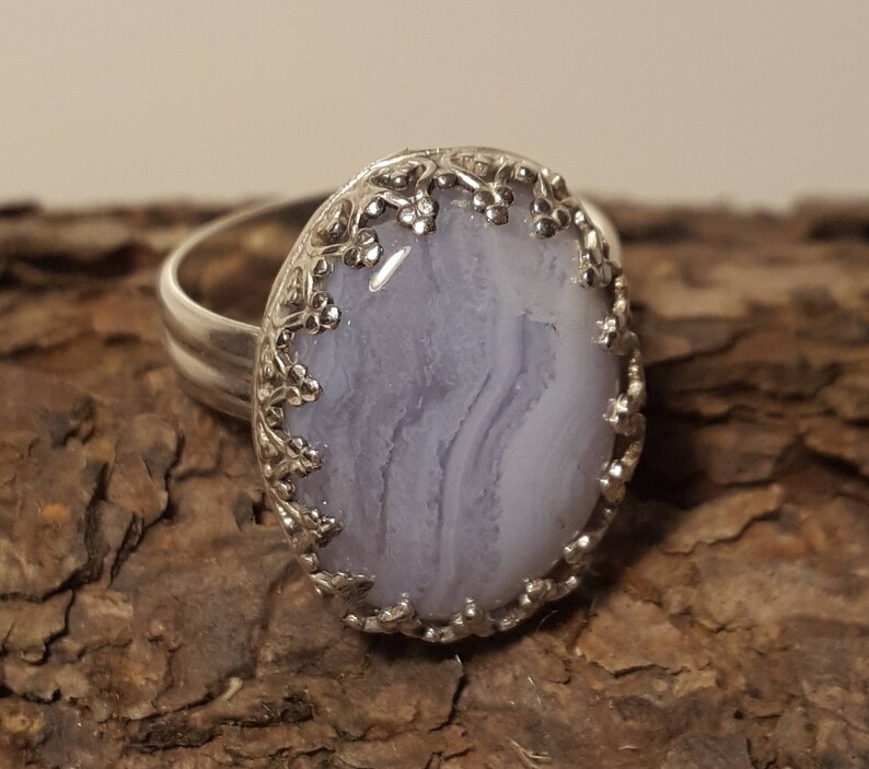 May include: A silver ring featuring a delicate floral design encircling a light blue agate stone.