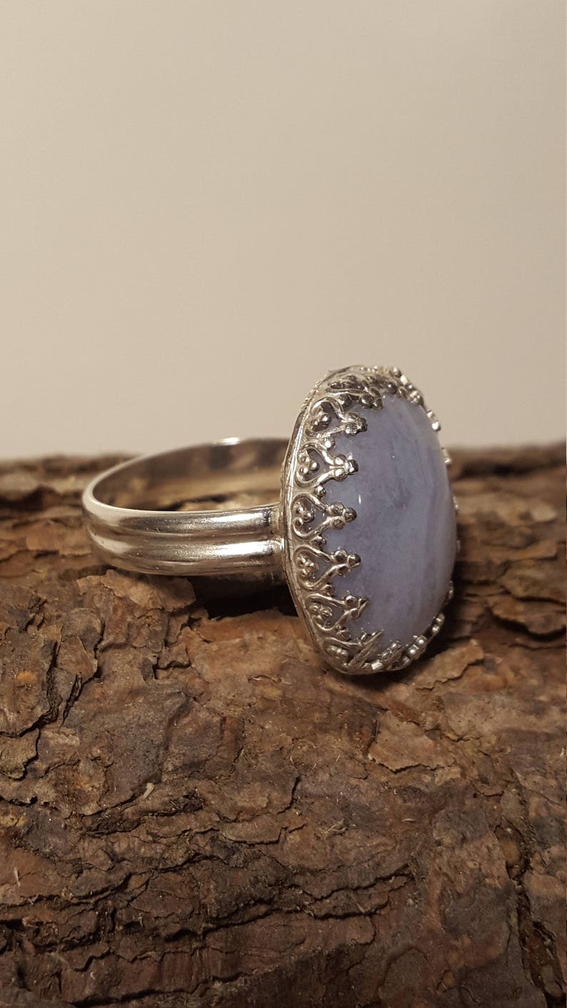 May include: A silver ring featuring a light blue oval gemstone set in an ornate silver bezel. The ring has a wide band.