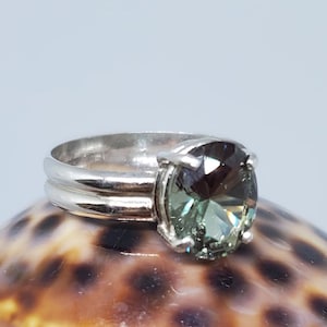 May include: A silver ring with a large, round, green gemstone. The gemstone has a faceted cut and a dark green color with hints of blue.