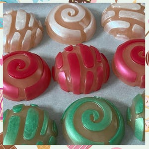 May include: Nine colorful, round, decorative soaps with various patterns, including swirls, stripes, and geometric designs. The soaps are arranged in a circular pattern on a white surface.