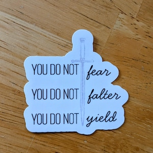 May include: A white sticker with the words "YOU DO NOT fear, YOU DO NOT falter, YOU DO NOT yield" in black and script font. A light purple sword illustration is in the center.