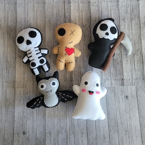 May include: Five felt Halloween character toys: a skeleton, a voodoo doll, a ghost, a bat, and a grim reaper. The toys are all handmade and have embroidered details.