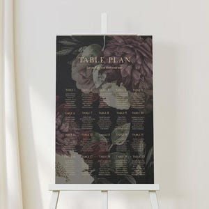 May include: A wedding table plan displayed on an easel. The plan features a dark background with floral accents and the words "TABLE PLAN" at the top. The plan lists table numbers and guest names in a classic font.