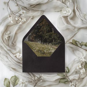 May include: A black envelope with a window showing a photograph of a forest clearing with white flowers.