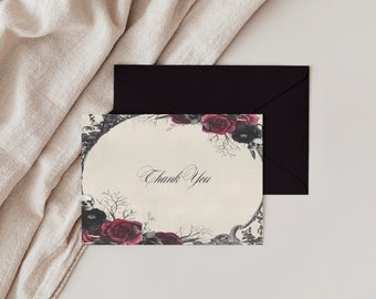 May include: A black and white thank you card with a circular frame of red roses, skulls, and branches. The text "Thank You" is written in black cursive inside the frame.