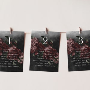 May include: Three dark gray table cards with floral designs and numbers 1, 2, and 3. Each card lists a set of names in white text.