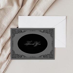 May include: A gray thank you card with a black oval in the center. The oval has a decorative black frame and the words "Thank You" written in white script.