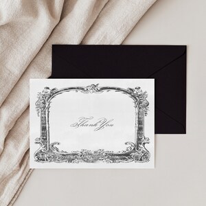 May include: A white thank you card with a black and white ornate frame. The text "Thank You" is written in cursive inside the frame.