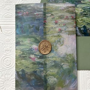 May include: An invitation suite featuring a watercolor painting of a pond with lily pads and pink flowers. The invitation is sealed with a gold wax seal. The suite includes an envelope with a green interior.
