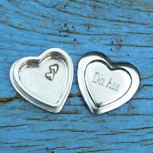 May include: Two silver heart-shaped boxes, one with a small heart-shaped indentation and the other with the inscription "Dix Ans".